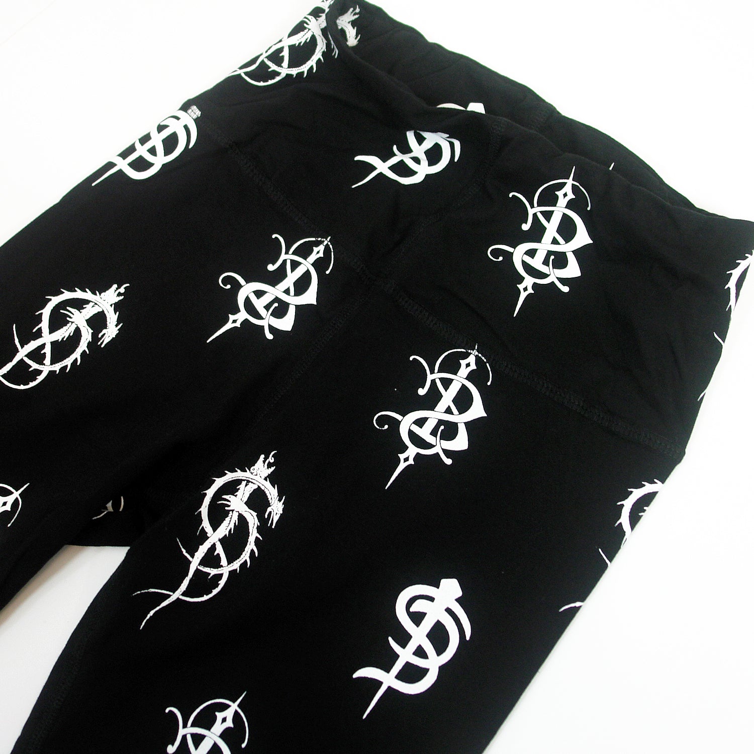 close up image of black leggings on a white background. leggings have white printed skinny puppy logos repeated all over